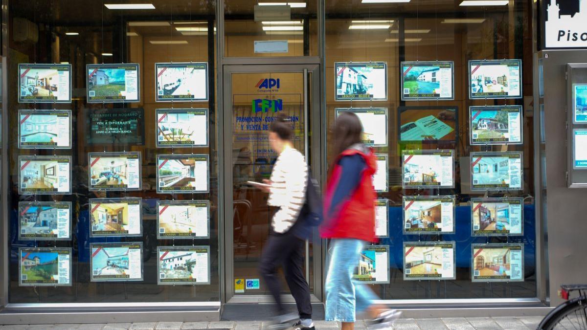 Dos jóvenes pasan ante el escaparate de una inmobiliaria en Gasteiz.