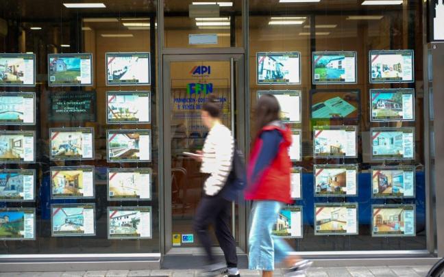 Dos jóvenes pasan ante el escaparate de una inmobiliaria en Gasteiz.