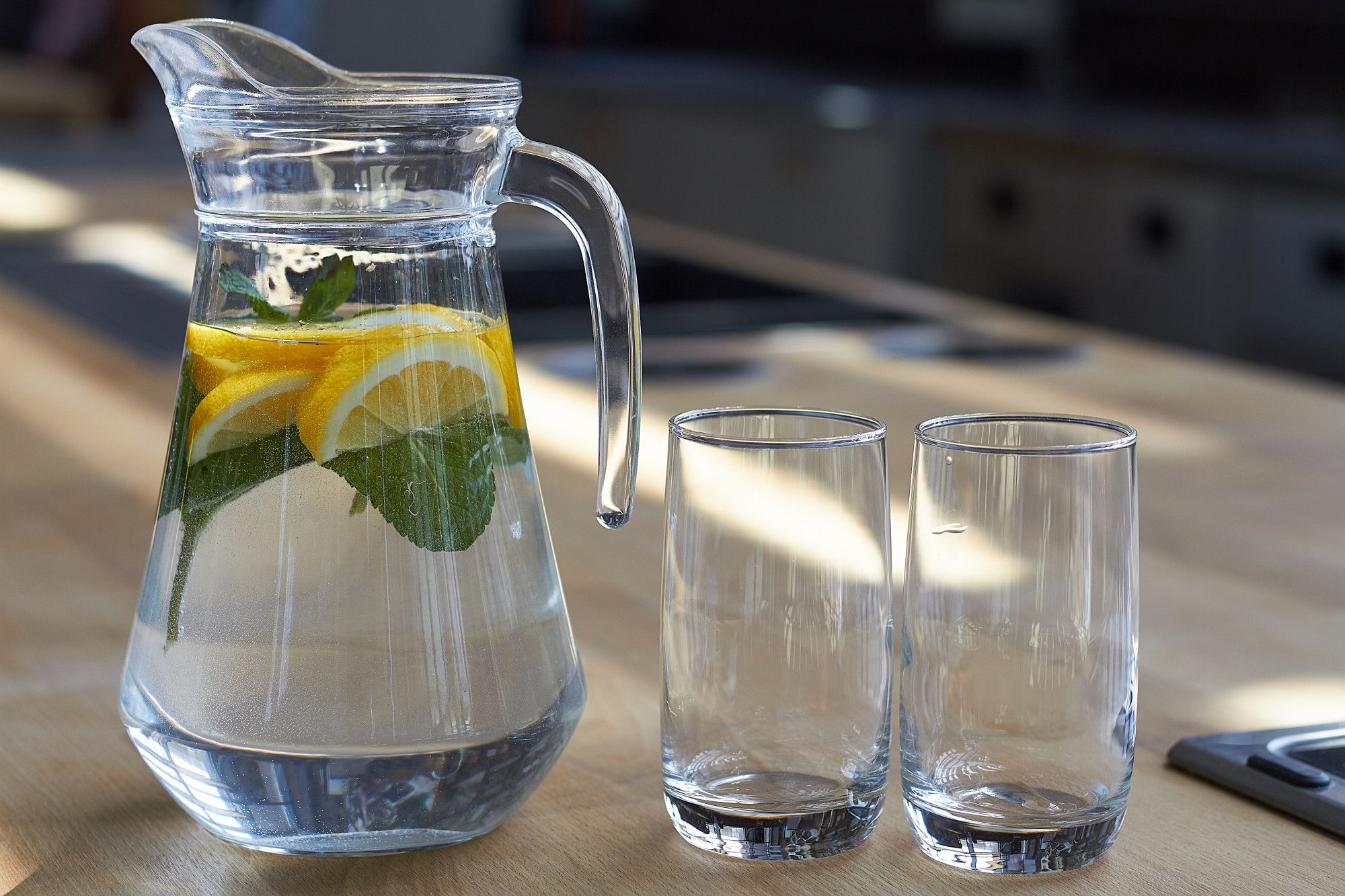 Una jarra de agua con rodajas de limón junto a dos vasos.