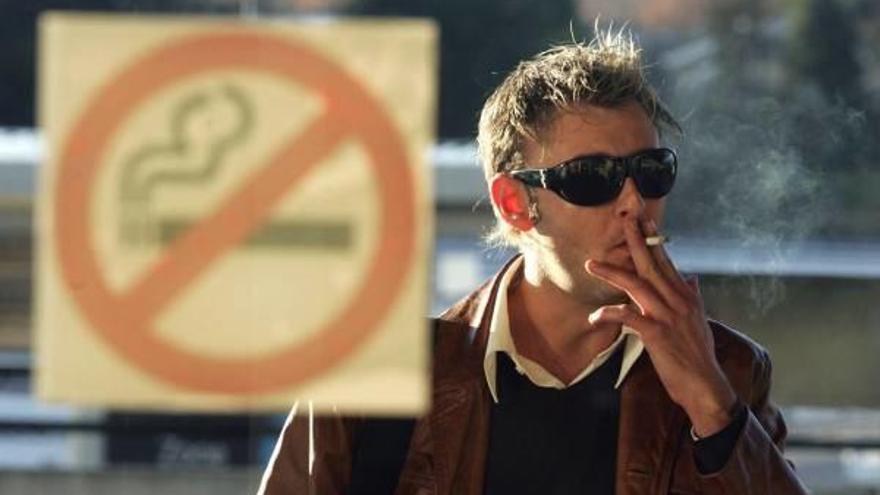 Un hombre fumando un cigarrillo en el exterior del local junto a un cartel que indica que está prohibido fumar en el interior.