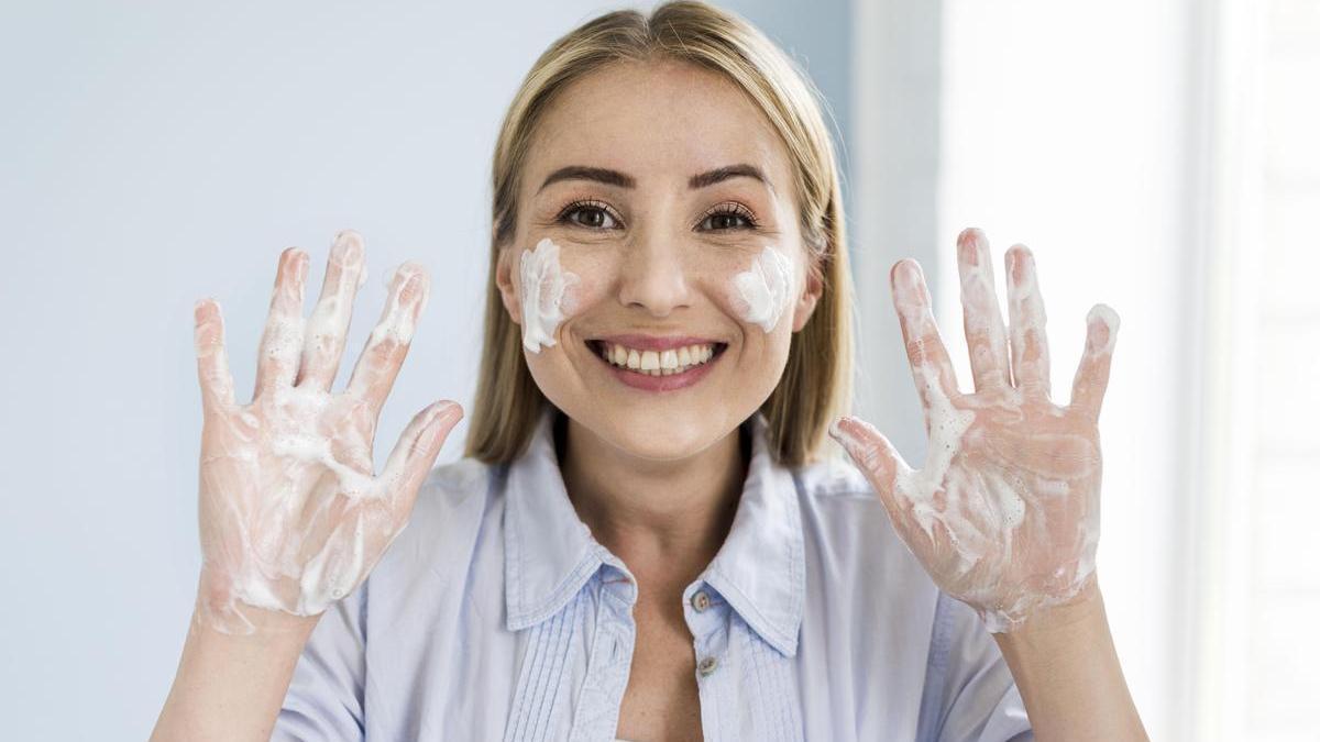 Mujer sonriente se lava la cara con un gel limpiador específico para su tipo de piel.