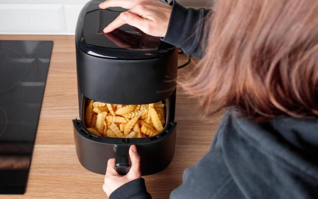 Una niña se está preparando unas patatas en la freidora.