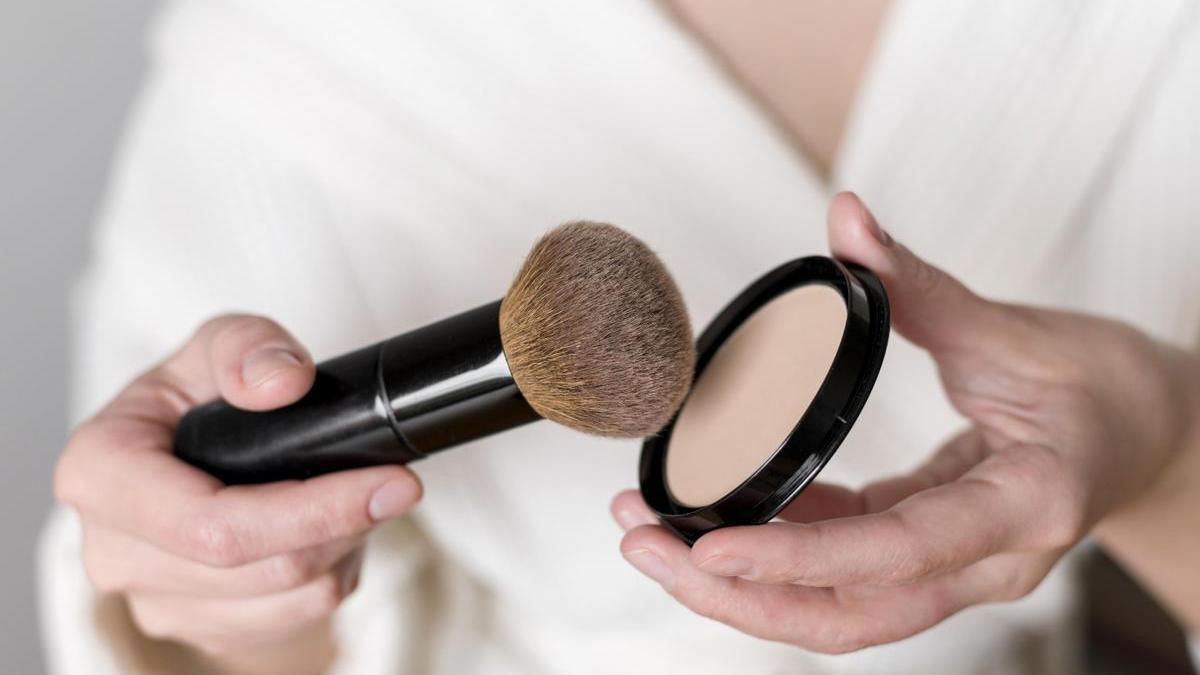 Primer plano de las manos de una mujer con una brocha y unos polvos de maquillaje.
