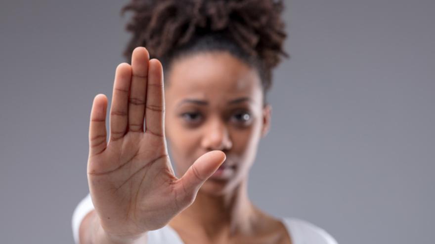 Attractive young African woman giving a halt or stop gesture with focus to the palm of her hand over a grey studio background (Attractive young African woman giving a halt or stop gesture with focus to the palm of her hand over a grey studio backgroun