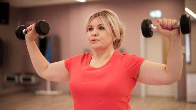 Una mujer hace entrenamiento de fuerza en un gimnasio.