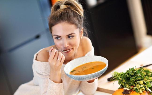 Una mujer toma un plato de sopa de calabaza. Una mujer toma un plato de sopa de calabaza.