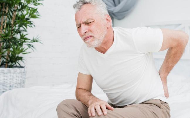 Un hombre con cara de dolor por una dolencia lumbar.