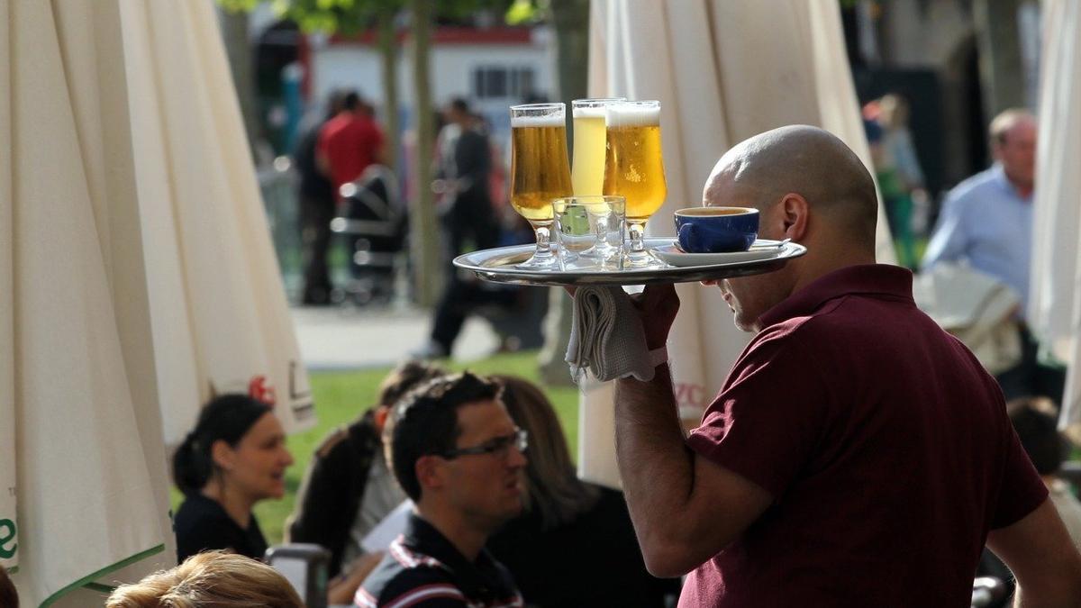 Un camarero sirve unas cervezas en la terraza de un bar.
