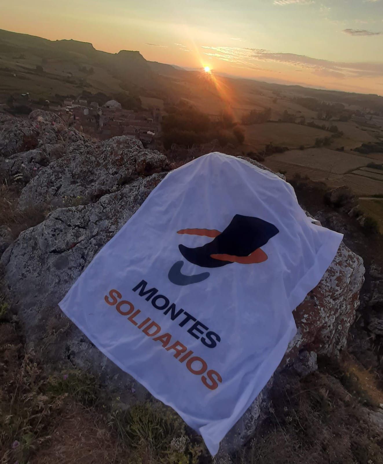 El logotipo de Montes Solidarios, en una cima al atardecer.