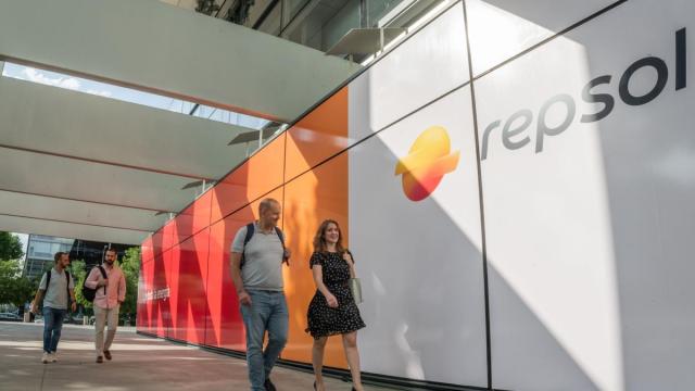 Empleados pasando por delante del panel de entrada a Campus con el nuevo logo de Repsol.