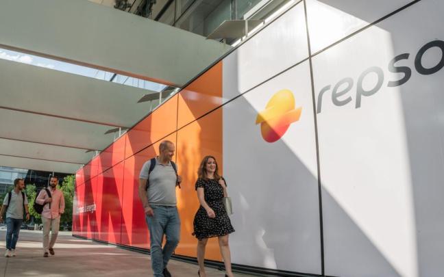 Empleados pasando por delante del panel de entrada a Campus con el nuevo logo de Repsol.