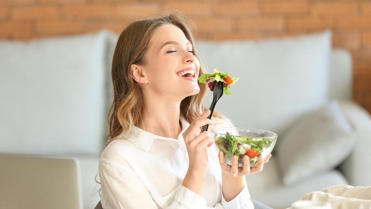 Mujer sonríe mientras come una ensalada.