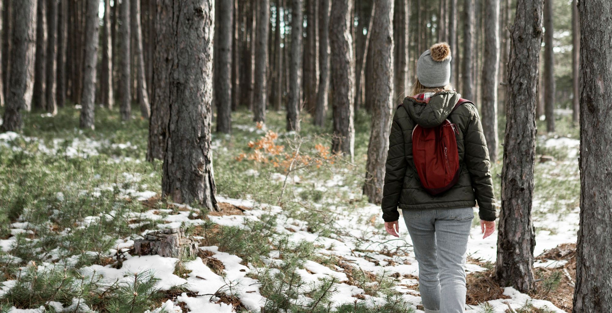 Una mujer camina abrigada por un bosque.