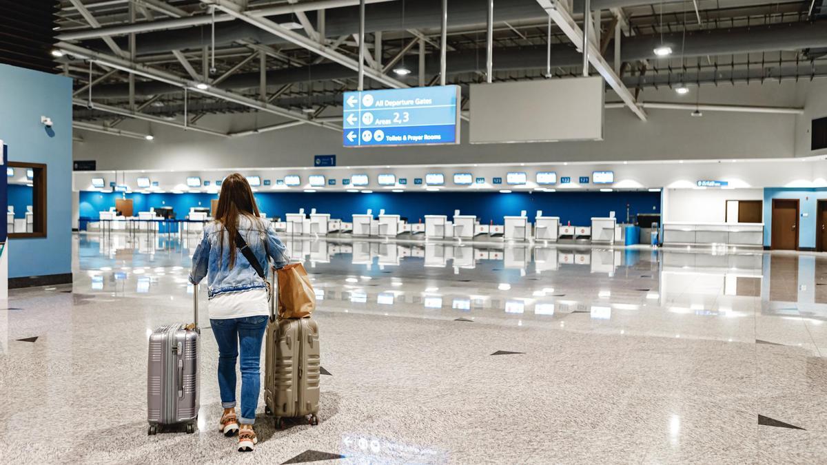 Una mujer camina por un aeropuerto con dos maletas.