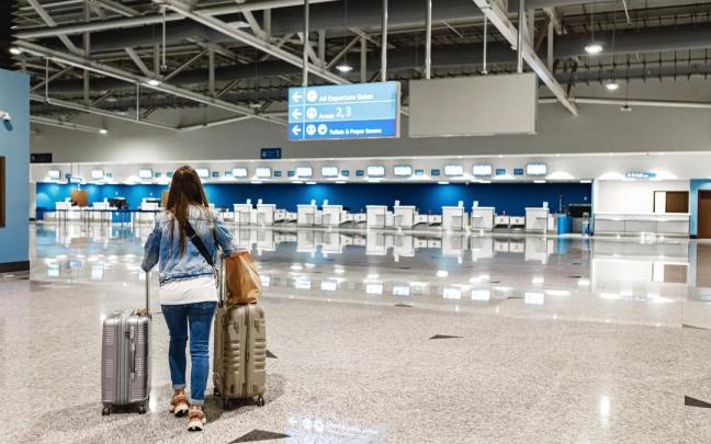 Una mujer camina por un aeropuerto con dos maletas.