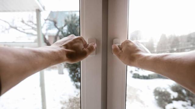 Un hombre abre las ventanas de su casa en invierno