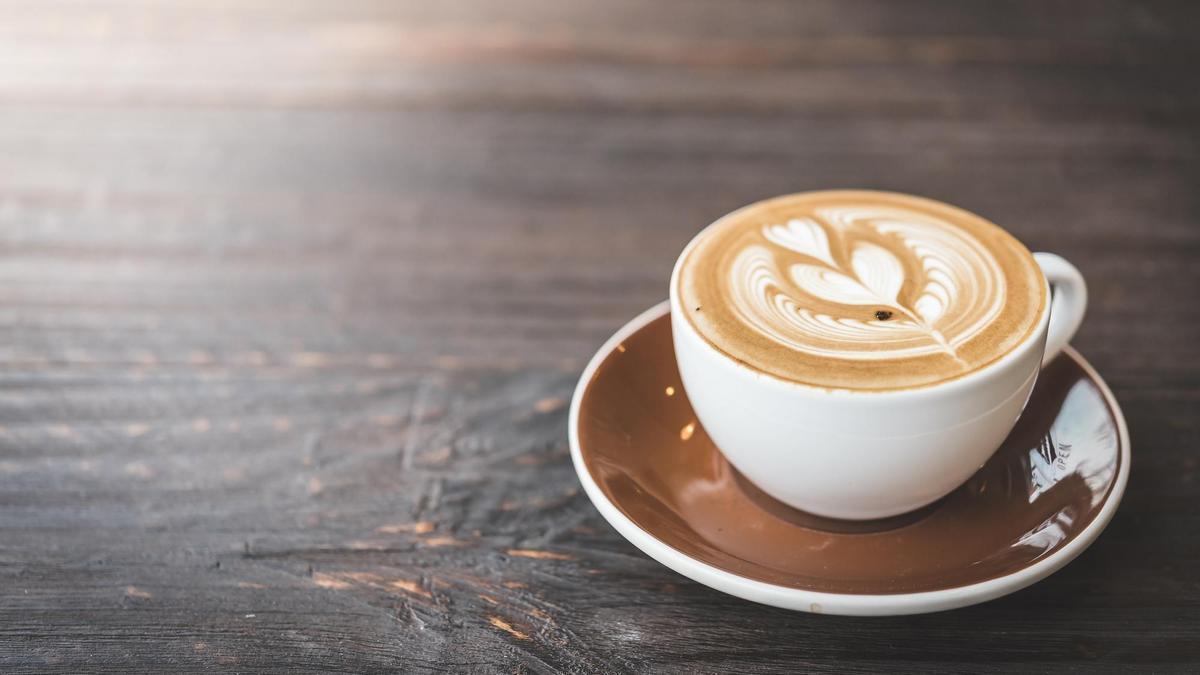 Una apetecible taza de café con leche con una flor dibujada en la espuma.