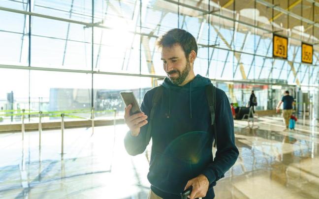 Un hombre camina por un aeropuerto con la maleta y el móvil en la mano. Un hombre camina por un aeropuerto con la maleta y el móvil en la mano.