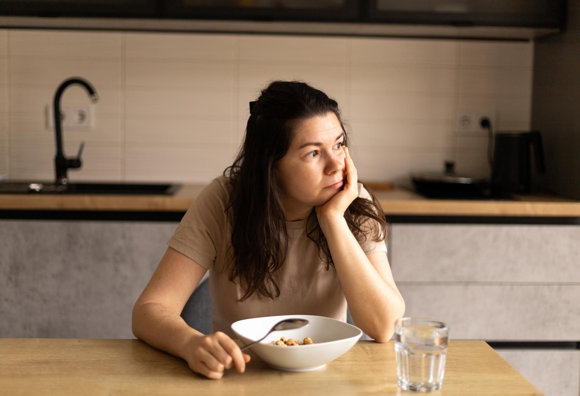 Una mujer, distraída delante de un plato de comida.