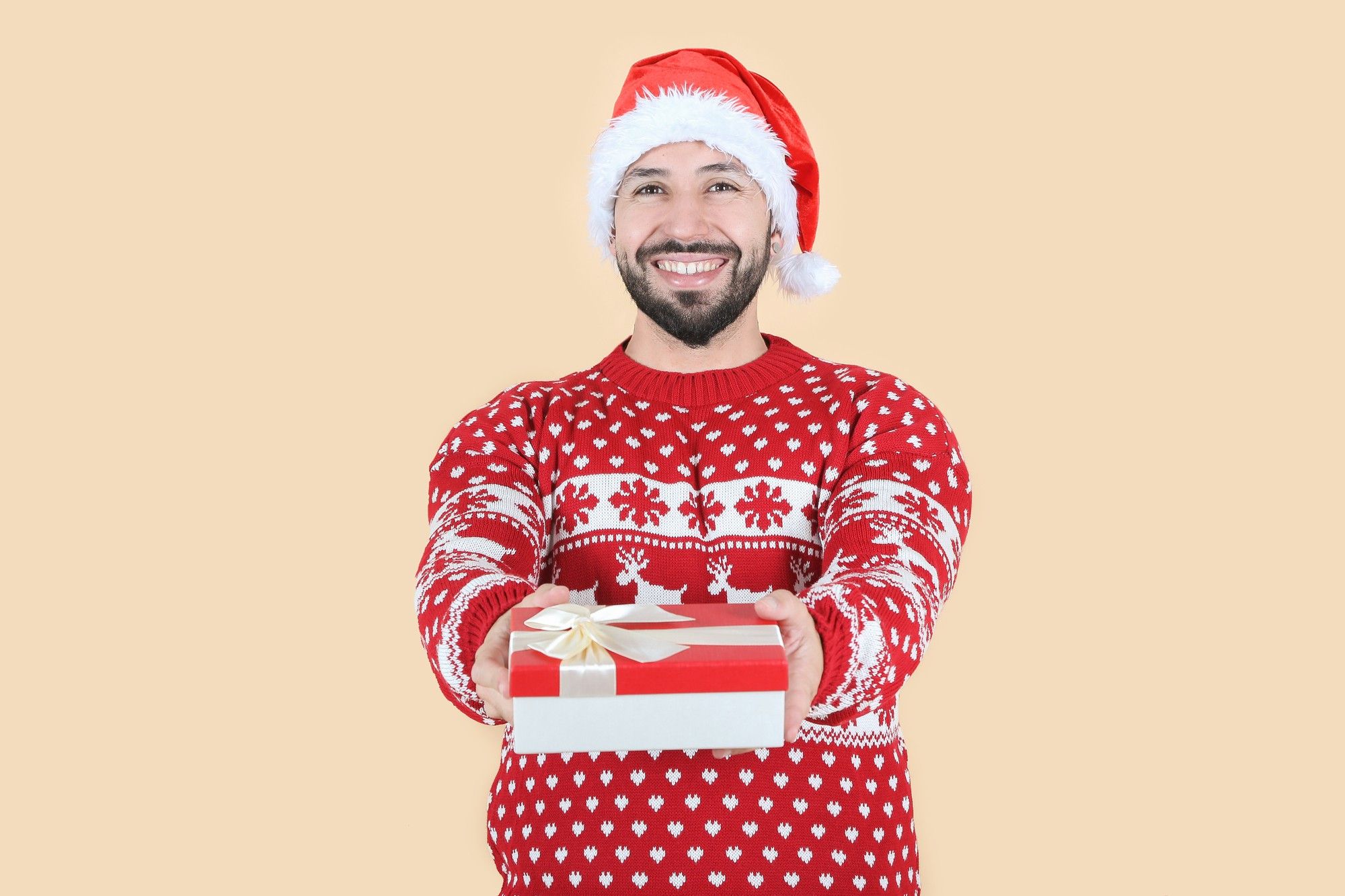 Un hombre sostiene un regalo vestido con un jersey con corazones, renos y copos de nieve.