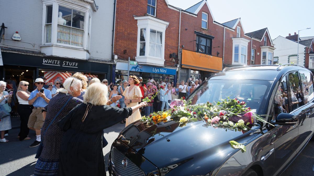 Varias personas lanzan flores al coche funerario que traslada los restos de Bonnie Tyler en Gales