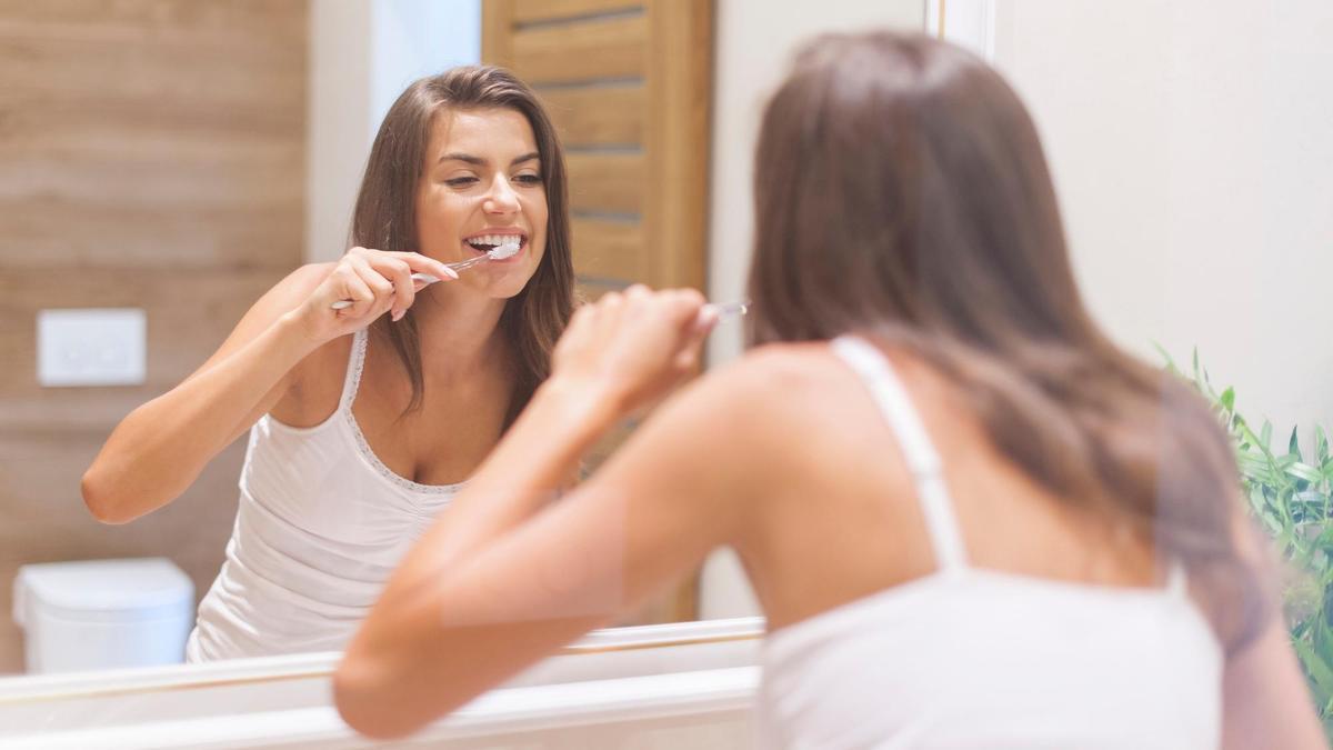 Una mujer se cepilla los dientes delante del espejo del baño.