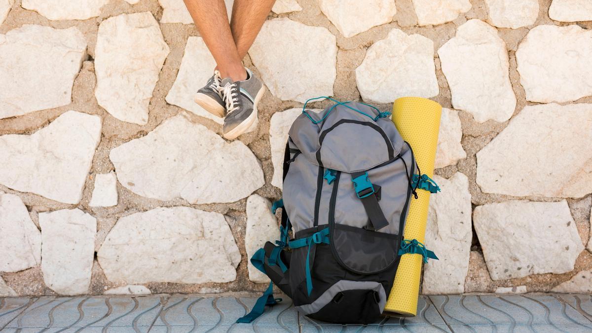 Persona sentada en un muro con su mochila apoyada en el suelo.