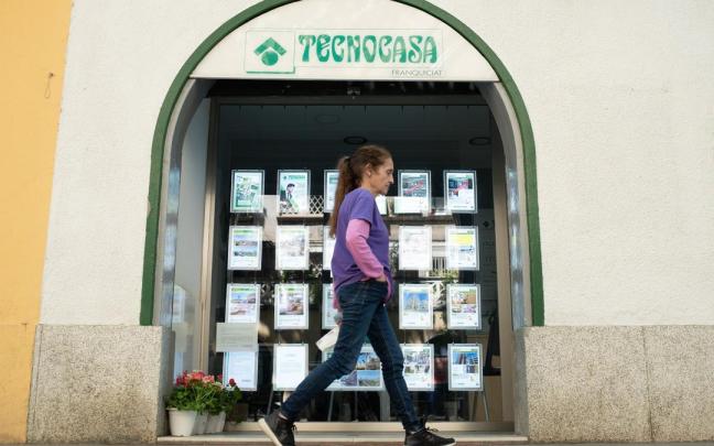 Una mujer pasa frente a una agencia inmobiliaria.