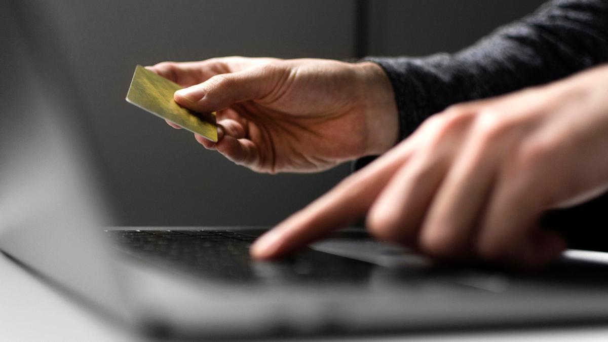 Un hombre introduce los datos de su tarjeta bancaria en un ordenador portátil.