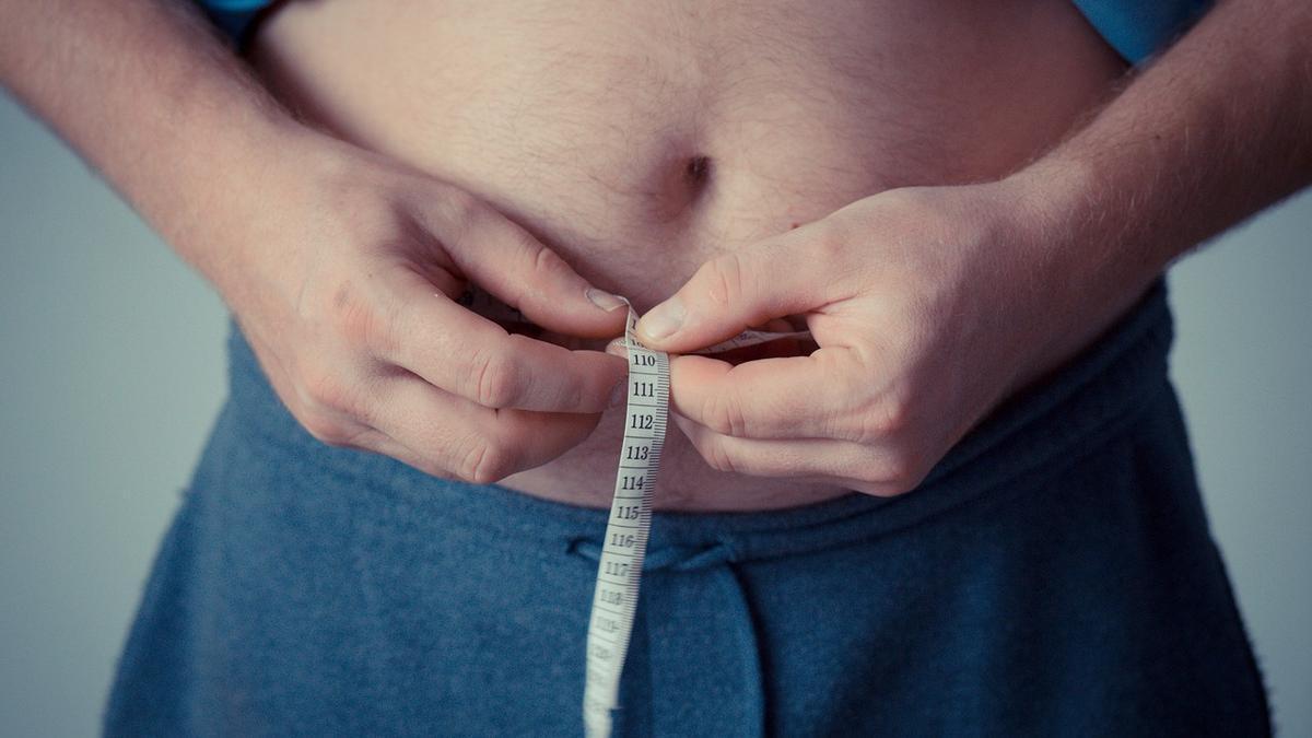 Un hombre que quiere adelgazar se mide la cintura con una cinta métrica.