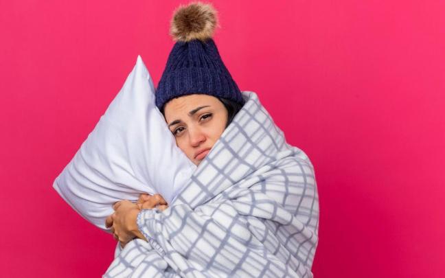 Una mujer con gorro de lana y envuelta en una manta se aferra a la almohada.