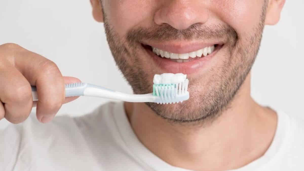 Hombre sostiene el cepillo de dientes delante del espejo del baño.