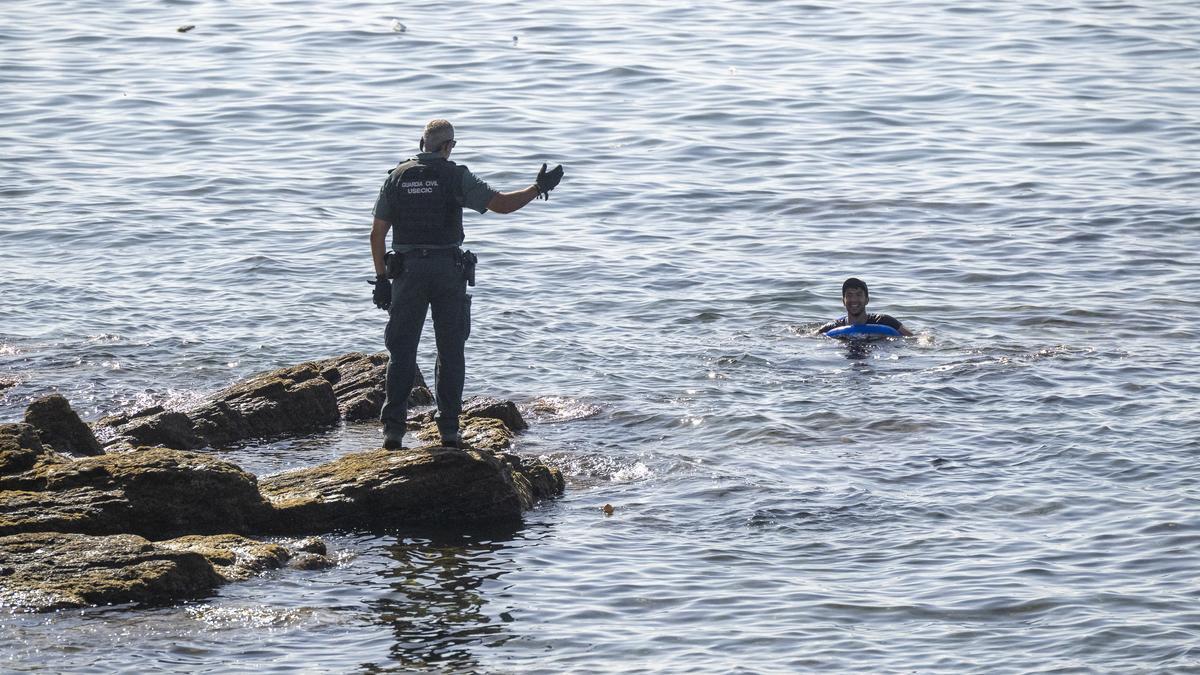 Un guardia civil advierte a una persona que permanece en el mar, en la frontera del Tarajal.