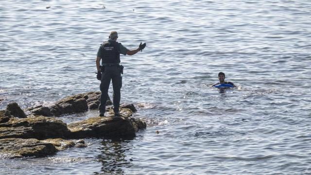 Un guardia civil advierte a una persona que permanece en el mar, en la frontera del Tarajal.