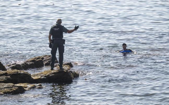 Un guardia civil advierte a una persona que permanece en el mar, en la frontera del Tarajal.
