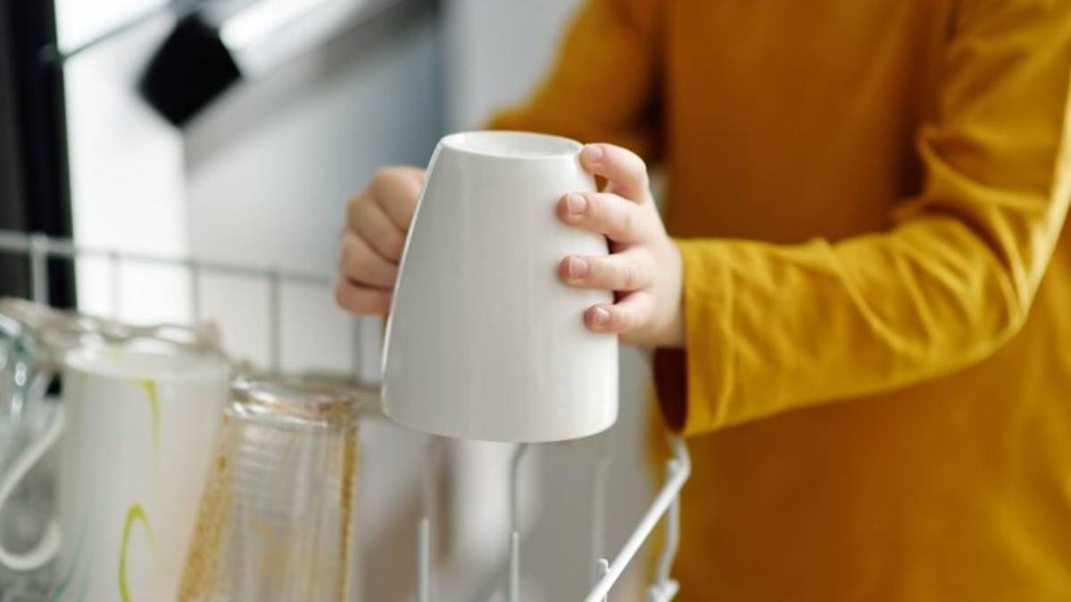 Manos de un niño colocando una taza blanca boca abajo en el lavavajillas