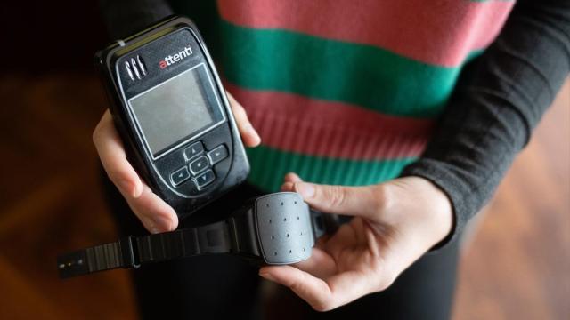 Una persona muestra una pulsera electrónica de geolocalización telemática y su monitor.