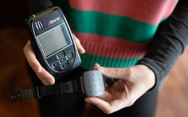 Una persona muestra una pulsera electrónica de geolocalización telemática y su monitor.