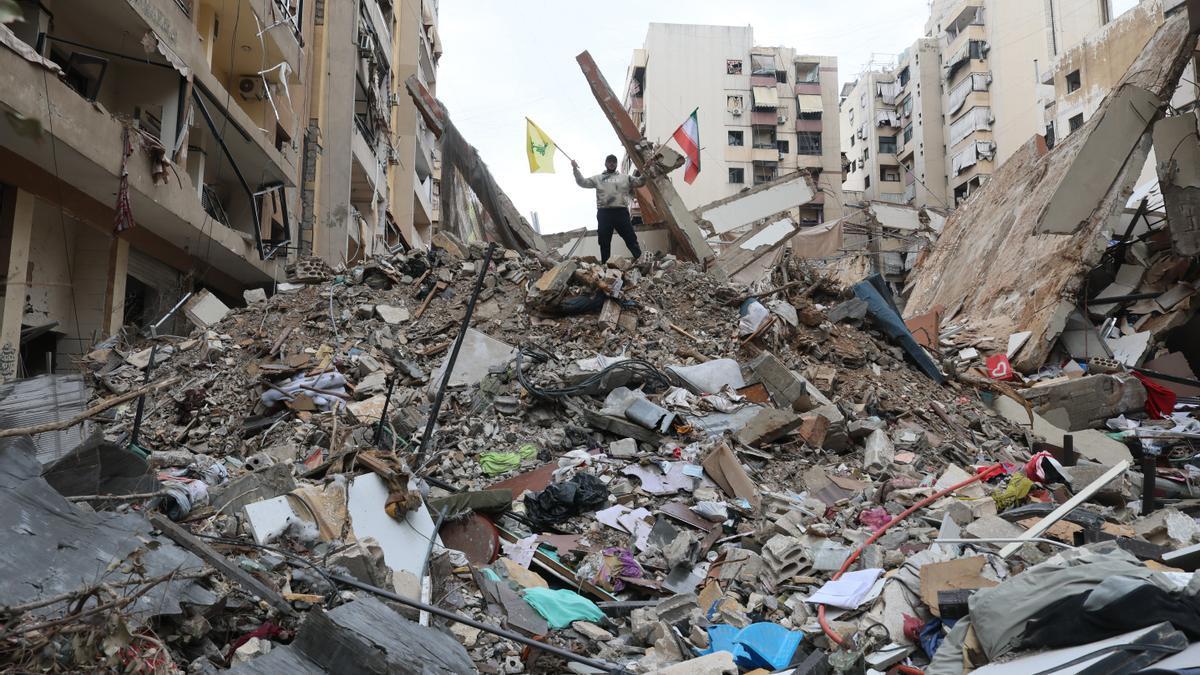 Un hombre ondea las banderas de Irán (derecha) y Hizbulá (izquierda), sobre los escombros de un edificio destruido por un ataque aéreo israelí en Beirut.