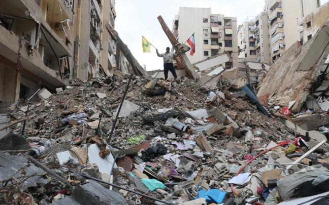Un hombre ondea las banderas de Irán (derecha) y Hizbulá (izquierda), sobre los escombros de un edificio destruido por un ataque aéreo israelí en Beirut.
