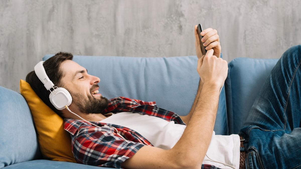 Un hombre se relaja escuchando música tumbado en el sofá.