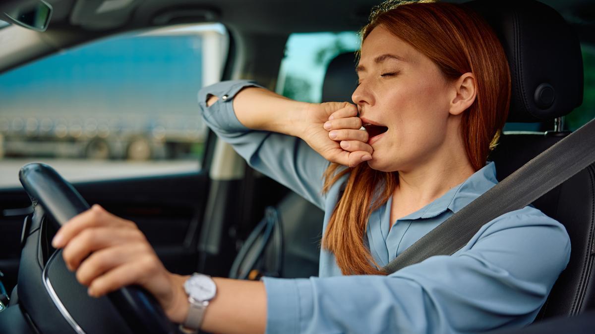 Una mujer bosteza mientras conduce su coche.