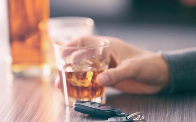 Una persona, bebiendo alcohol con las llaves del coche sobre la mesa.