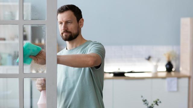 Un hombre limpia el cristal de una puerta con una bayeta.