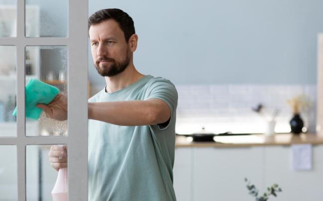 Un hombre limpia el cristal de una puerta con una bayeta.
