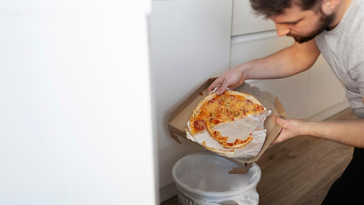 Un hombre tira más de media pizza a la basura.
