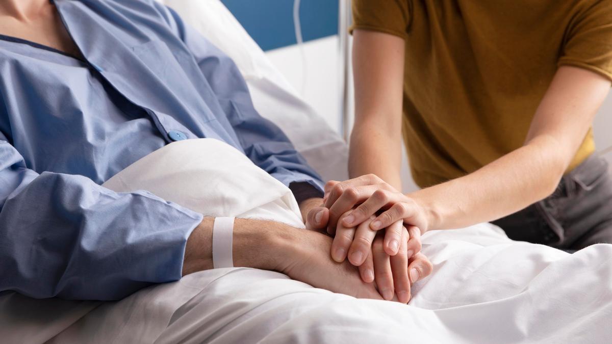 Una persona entrelaza sus manos con las de un familiar hospitalizado.
