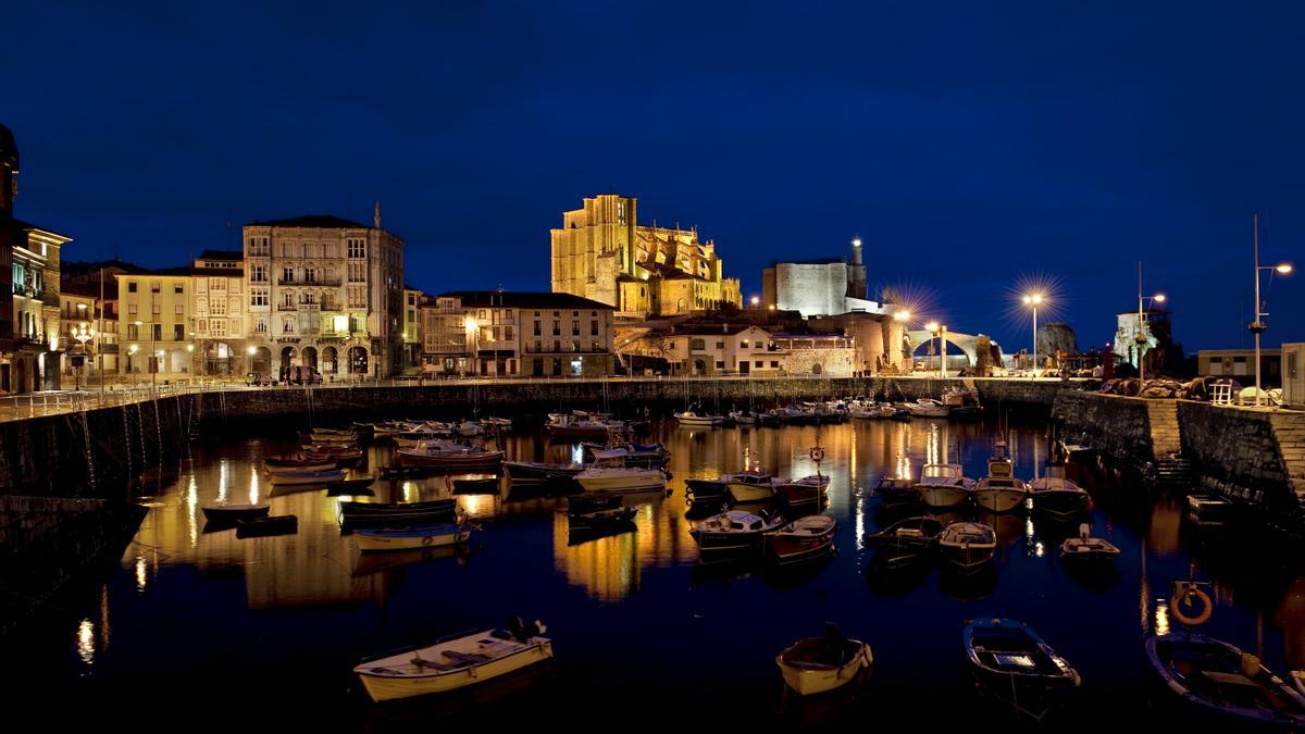 Vista nocturna del castillo de Santa Ana con el faro encendido y la iglesia de la Asunción iluminada.