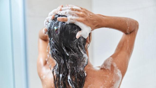 Mujer de espaldas se lava el pelo en la ducha.