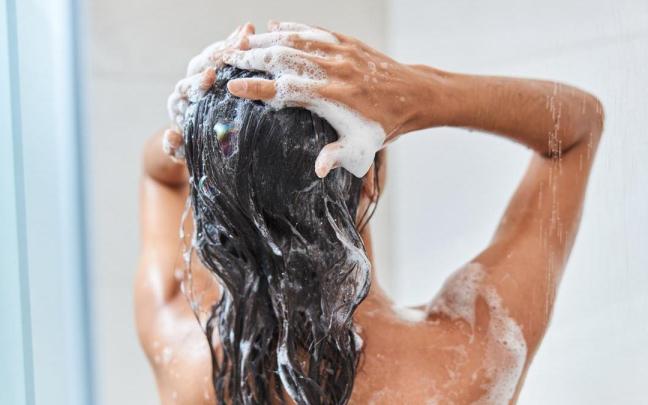 Mujer de espaldas se lava el pelo en la ducha.